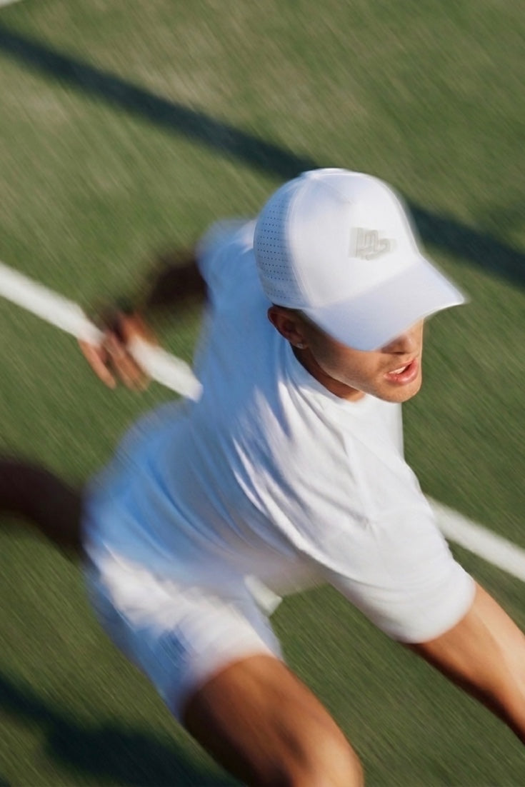 LUPPO white performance polyester hat with laser-perforated side panels and curved brim, worn by a tennis player.